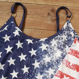 Woman wearing a sleeveless dress with distressed American flag print, taking a mirror selfie with stars on one side and red stripes on the other.

